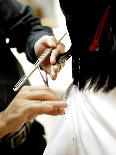 Ein Friseur schneidet das Haar einer Kundin. Der Friseur verwendet eine Schere und einen Kamm.