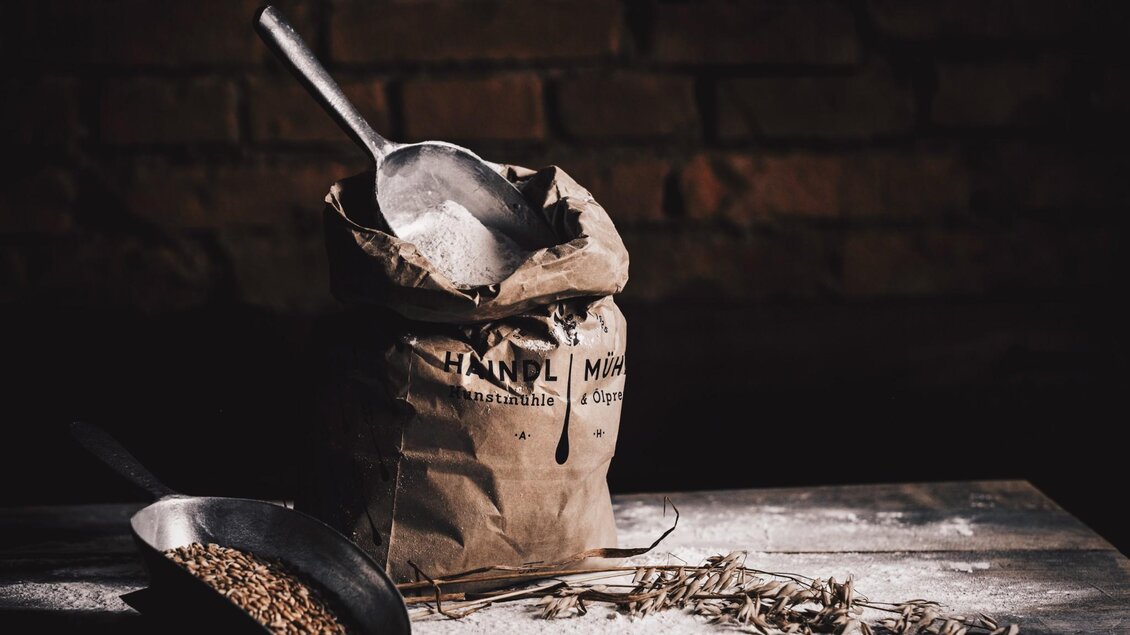Mehlsack der Haindl-Mühle mit Schaufel, Getreidekörnern und Ähren auf Holztisch | © ee photograph - Elena Egger