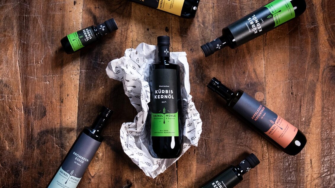 Verschiedene Flaschen mit Kürbiskernöl, Essig und Öl aus der Haindl-Mühle auf Holztisch | © ee photograph - Elena Egger