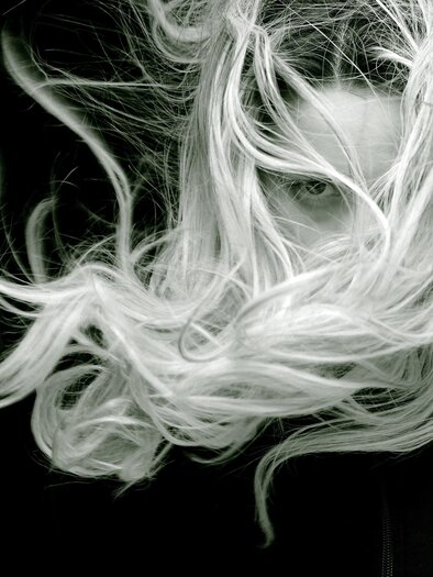 A mysterious portrait of a person with long, flowing hair. The background is black, enhancing the contrast with the hair color. | © Hairg'richt am Platzl