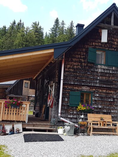 Eine gemütliche Holzhütte umgeben von Bäumen und Wiese. Der Eingang ist einladend mit bunten Blumen dekoriert. | © Rotsohlalm