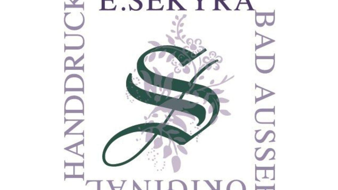 Ein Handwerker arbeitet an einem bunten Stoffmuster mit einer Holzform. Die Hände sind konzentriert an der Arbeit, während der Stoff auf dem Tisch liegt. | © Handdrucke Sekyra-Helge Kirchberger