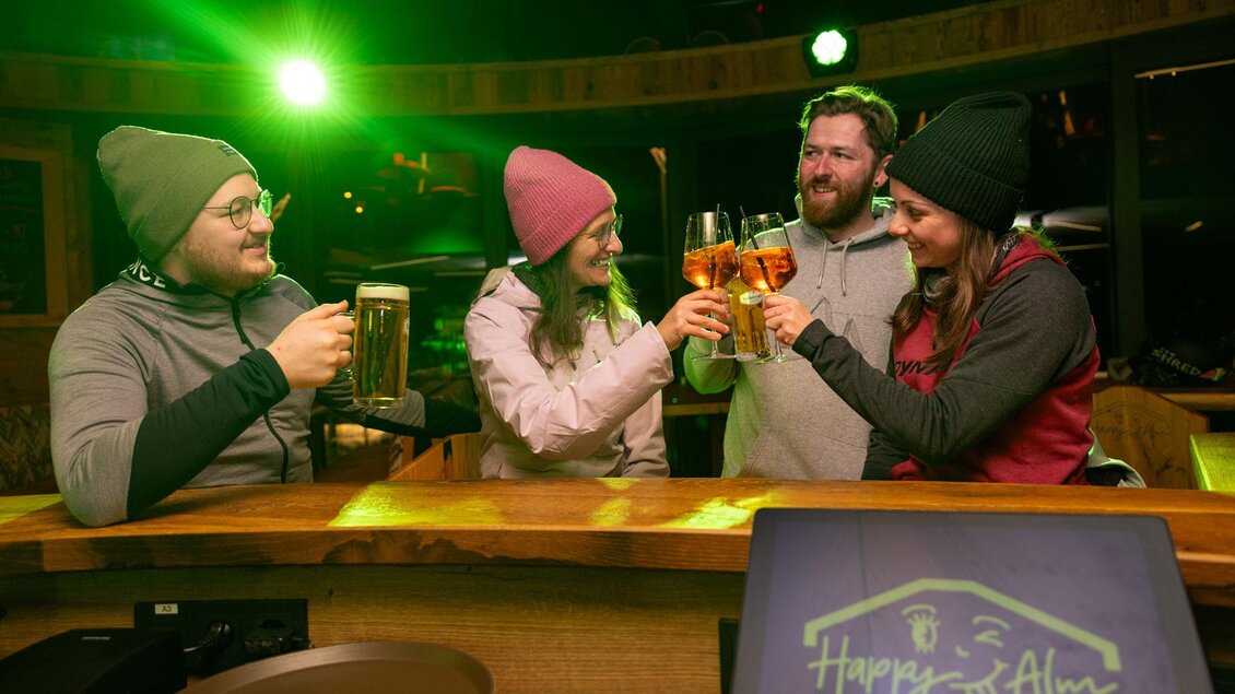 Eine Gruppe von vier Personen hebt ihre Gläser in einem gemütlichen Barambiente an. Alle tragen Mützen und genießen den Moment gemeinsam. | © Harald Steiner