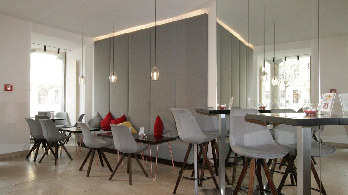 Ein modernes Café mit stilvollen, grauen Stühlen und kleinen Tischen. Große Fenster bieten viel Licht und eine einladende Atmosphäre. | © Haus 4