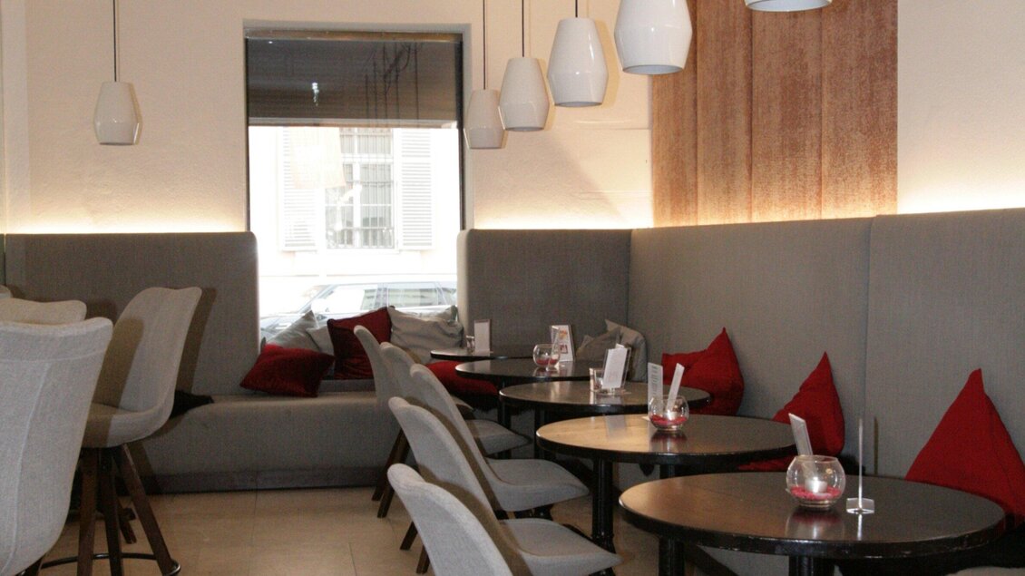 Ein modernes Café mit gemütlichen Sitzgelegenheiten und warmen Farben. Die Tische sind mit kleinen Kerzen dekoriert, und die Wände sind hell beleuchtet. | © Haus 4