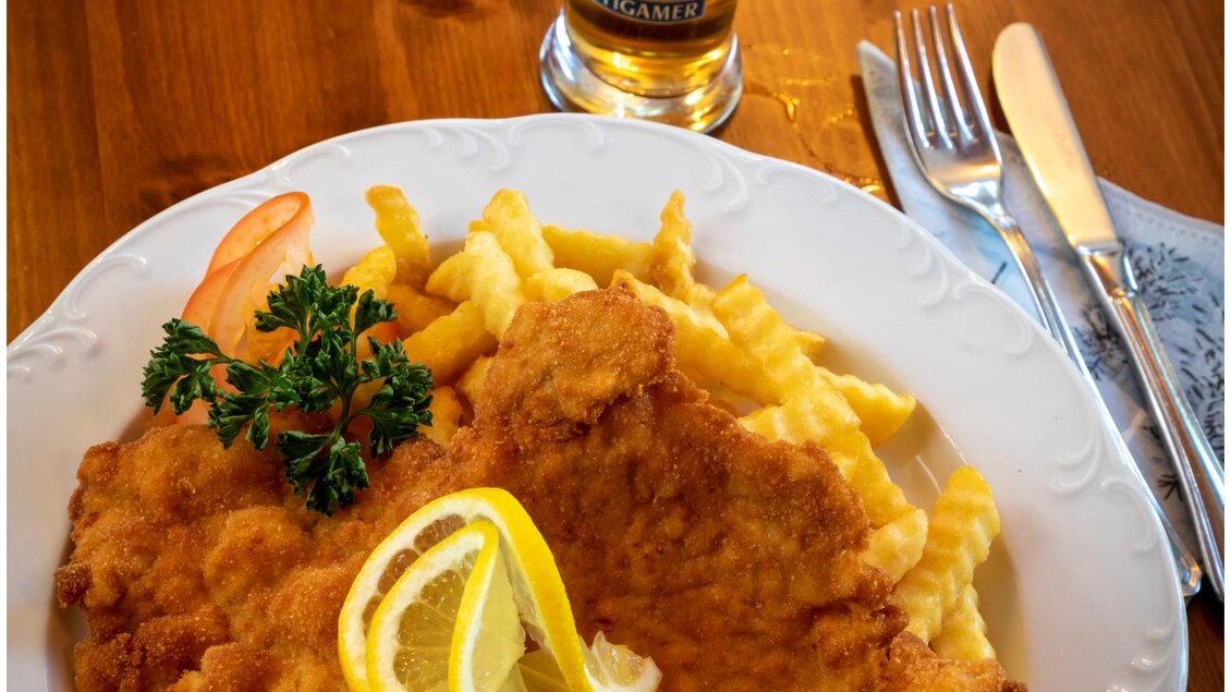 Ein köstliches Gericht mit paniertem Fisch, Pommes frites und einer Zitronenscheibe. Dazu ein Glas Bier auf einem Holztisch. | © TV Region Graz - Lunghammer