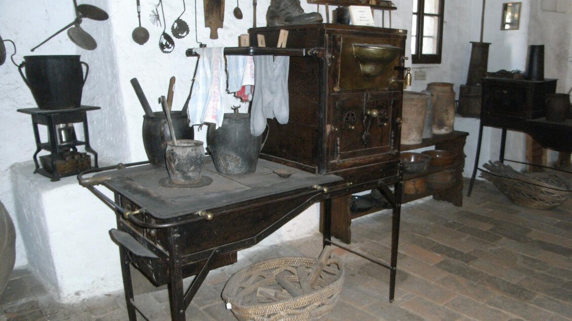 Eine alte Küche mit Holzmöbeln und verschiedenen Kochutensilien. An der Wand hängen Töpfe und Werkzeuge, die zur Zubereitung von Speisen verwendet werden. | © Stadtgemeinde Feldbach