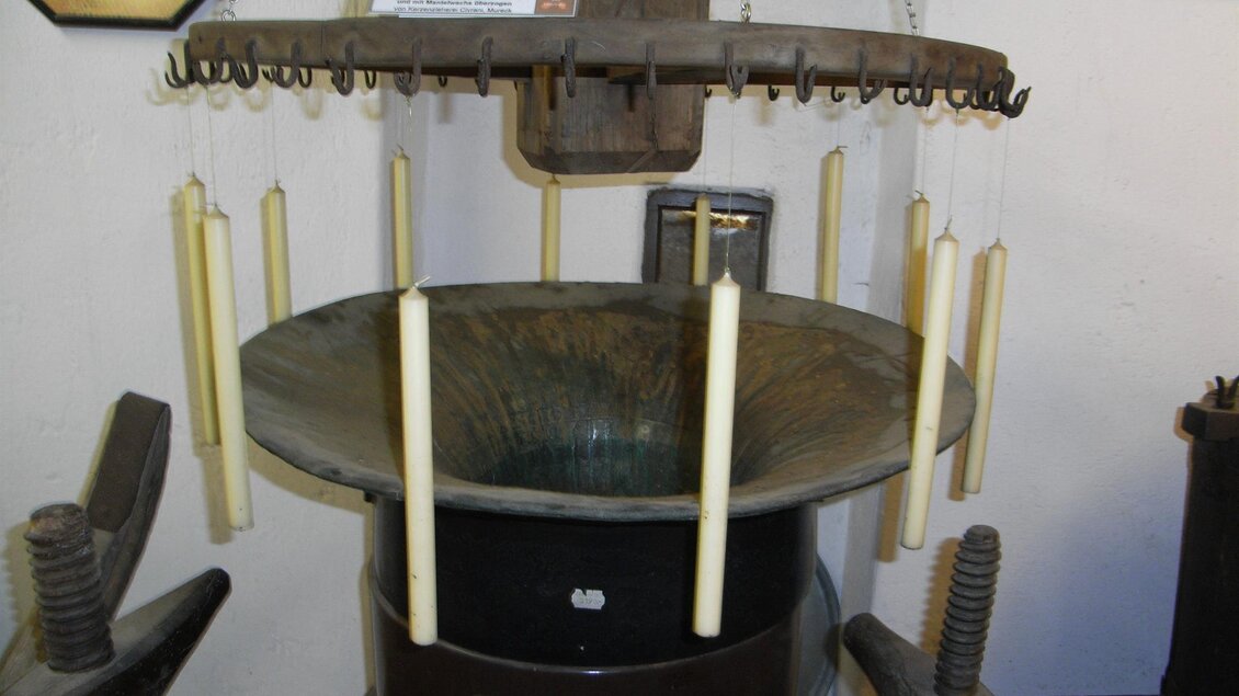 Eine historische Wachskerze-Herstellungsmaschine mit mehreren hängenden Kerzenformen. Die Maschine zeigt die traditionellen Techniken zur Kerzenproduktion. | © Stadtgemeinde Feldbach