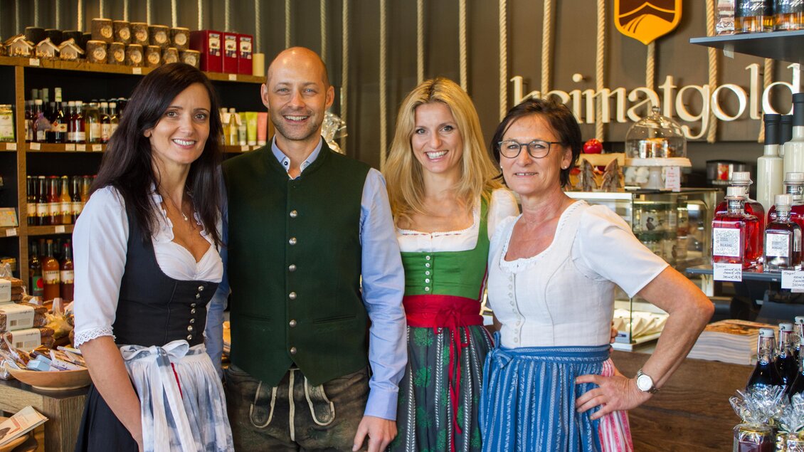 Eine Gruppe von vier Personen in traditioneller Tracht steht in einem Geschäft. Im Hintergrund sind verschiedene Produkte ausgestellt. | © Heimatgold