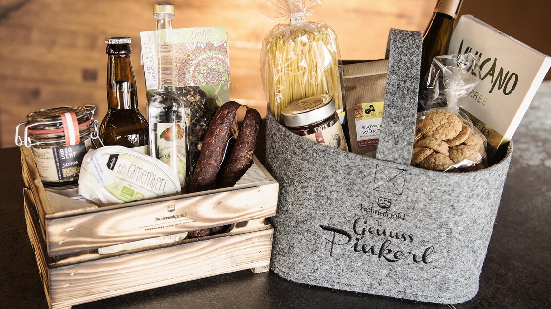 Ein Geschenkkorb mit verschiedenen Lebensmitteln und Getränken, darunter Pasta, Gewürze und Snacks. Die Produkte sind ansprechend in Holz- und Filzbehältern angeordnet. | © Heimatgold