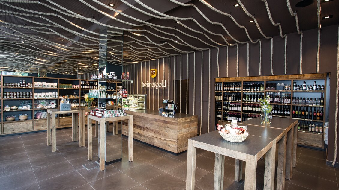 Ein modernes Geschäft mit Holztischen und Regalen voller Produkte. Die Wände sind stilvoll mit geschwungenen Linien gestaltet. | © Heimatgold