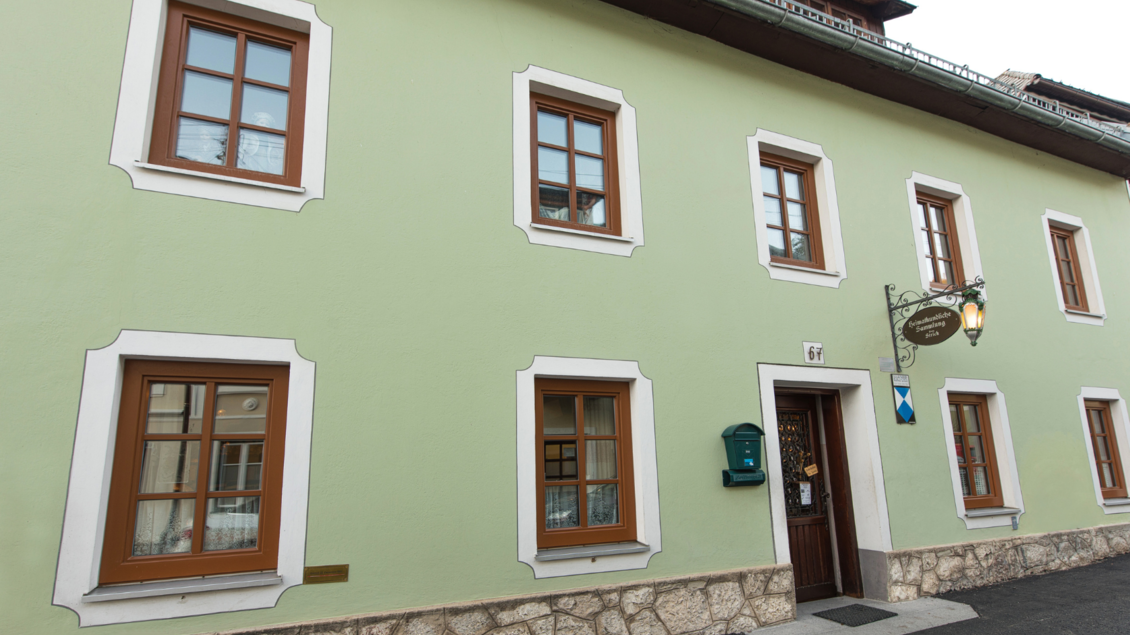Ein charmantes, hellgrün gestrichenes Gebäude mit braunen Fensterrahmen. Die Fassade hat eine steinerne Basis und mehrere Fenster, die einladend wirken. | © Stephan Pelizzari