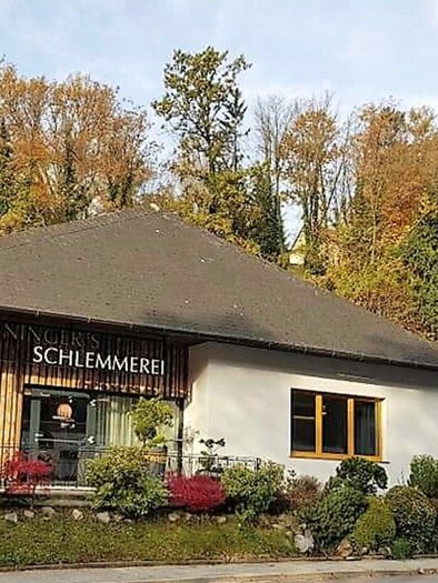 Ein gemütliches Restaurant mit dem Namen "Schlemmerei" in einer herbstlichen Umgebung. Bunte Blätter und grüne Pflanzen umgeben das Gebäude. | © Heiningers Schlemmerei