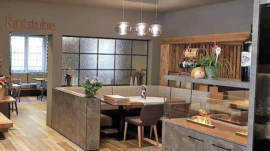 Ein modern eingerichteter Restaurantbereich mit Holz- und Betonelementen. Am Tisch stehen Pflanzen und es gibt gemütliche Sitzgelegenheiten. | © Heiningers Schlemmerei