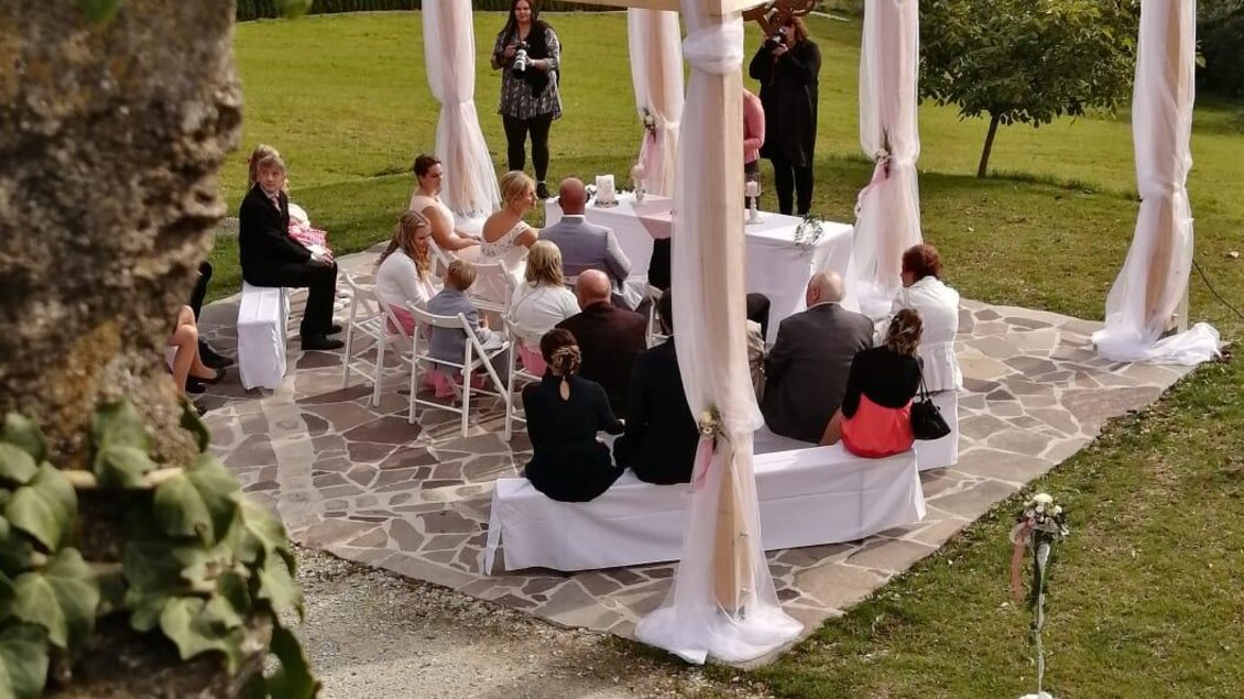 Eine Hochzeit im Freien unter einem dekorierten Pavillon. Die Gäste sitzen auf weißen Stühlen und genießen die Aussicht auf die grüne Landschaft. | © Standesamt Friedberg