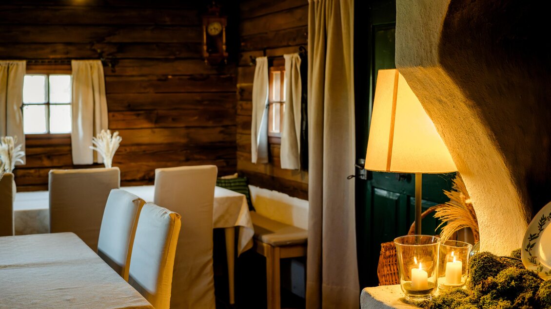 Ein gemütlicher Raum mit Holzwänden und einem warmen Licht. Es gibt einen Tisch mit weißen Stühlen und dekorative Kerzen. | © Region Graz - Mias Photoart