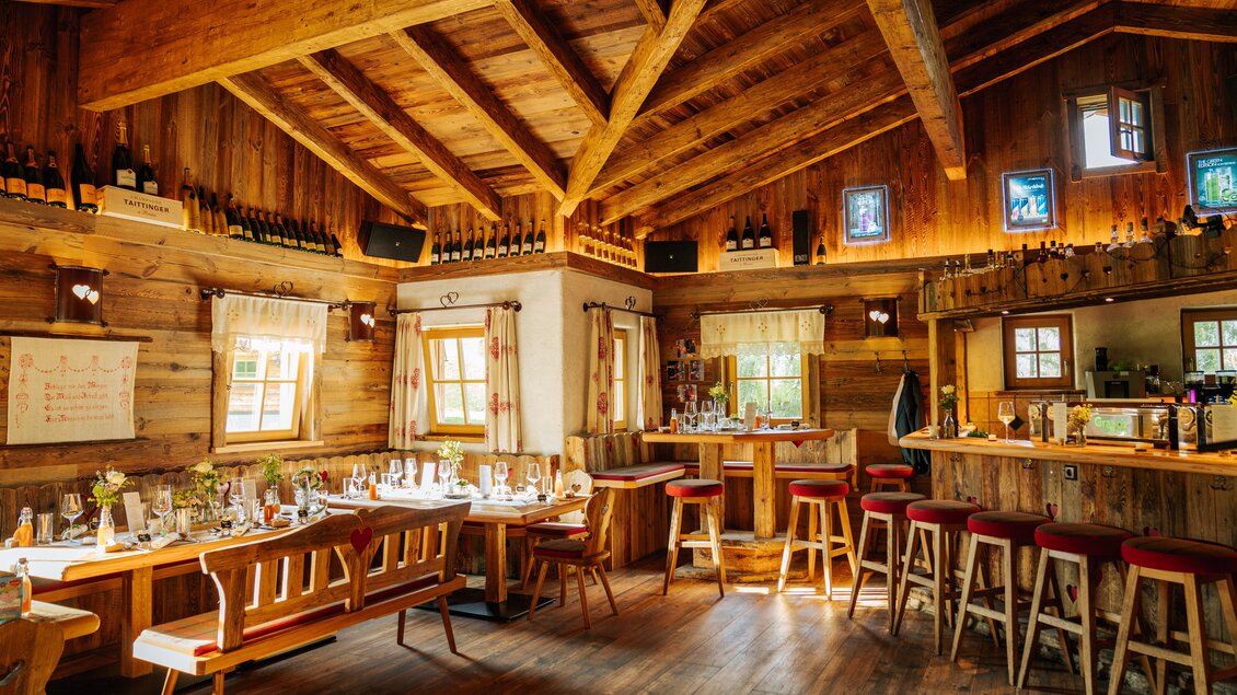 Ein gemütliches Restaurant mit einem rustikalen Holzdach. Holztische und Stühle sind elegant dekoriert, und die Bar lädt zum Verweilen ein. | © Strasser