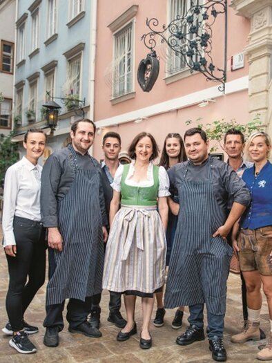 A group of people is standing in a picturesque alley. They are wearing traditional clothing and smiling warmly at the camera. | © Netzwerk Kulinarik