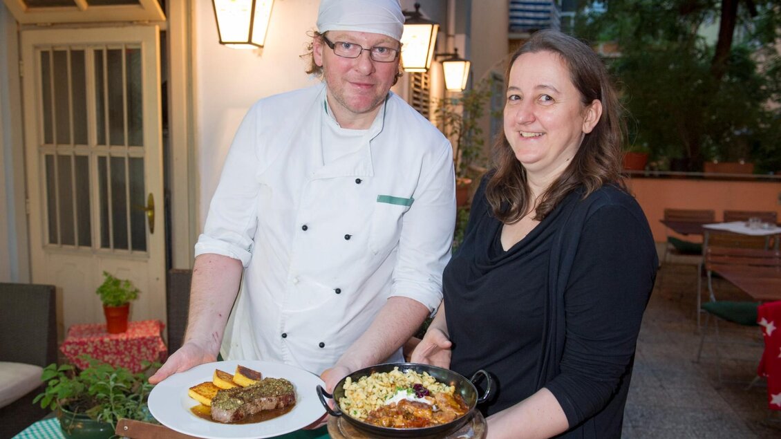 Ein Koch serviert ein Gericht, während eine Frau ein anderes Gericht hält. | © Herzl Weinstube