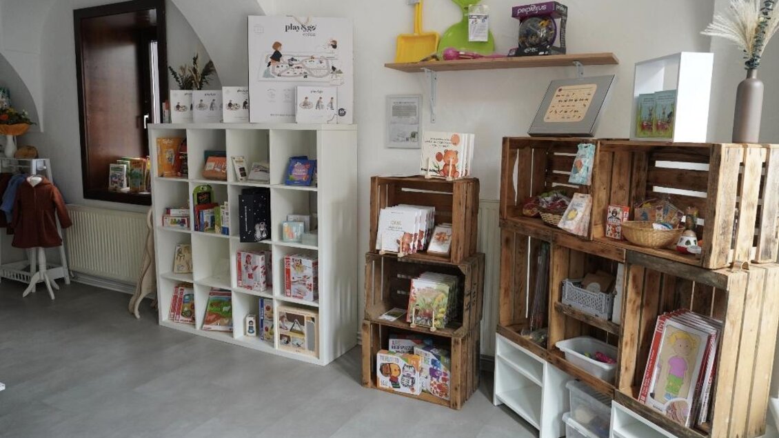 Ein helles Zimmer mit Regalen, die Bücher und Dekorationen zeigen. Auf der linken Seite sind weiße Regale und auf der rechten Seite Holzkisten. | © Denise Siedler