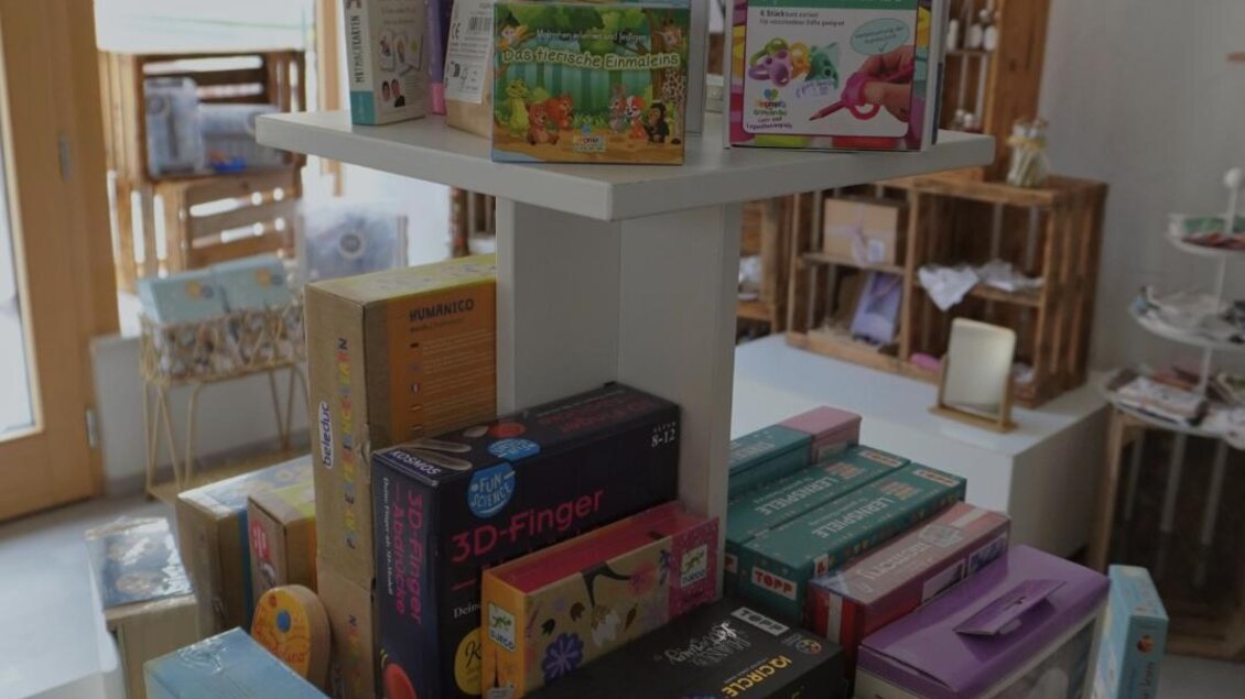 Ein stabiler Aufsteller mit bunten Kartons von Spielen und Puzzle. Im Hintergrund sind weitere Regale und Möbel sichtbar. | © Denise Siedler