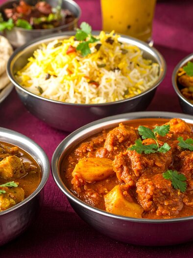 A traditional Indian thali with various dishes in small bowls. The background is dark red. | © Firefly - Benedikt Trummer