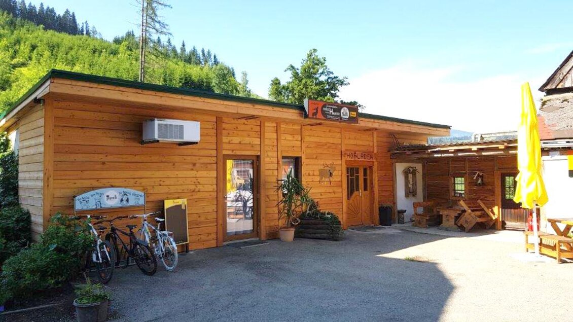 Ein gemütlicher Holzbauten mit einem kleinen Empfangsbereich. Draußen stehen Fahrräder und es gibt einen sonnigen Platz zum Entspannen. | © Hirschgehege Hauser