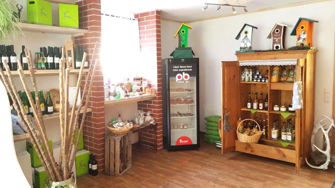 Ein kleiner Laden mit Regalen voller Flaschen und Lebensmitteln. Ein Holzschrank und ein Kühlschrank sind ebenfalls sichtbar. | © Hirschgehege Hauser