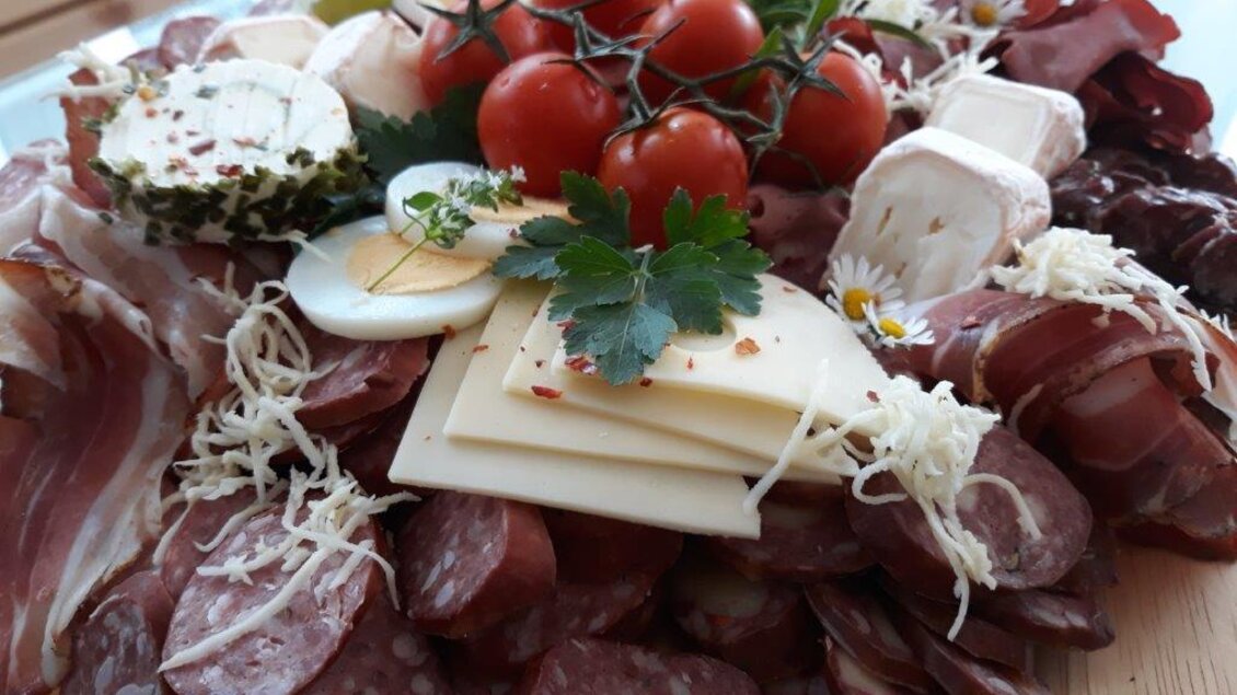 Eine Platte mit einer Auswahl an Wurst, Käse und frischen Tomaten. Dekoriert mit frischen Kräutern und Trauben. | © Hirschgehege Hauser