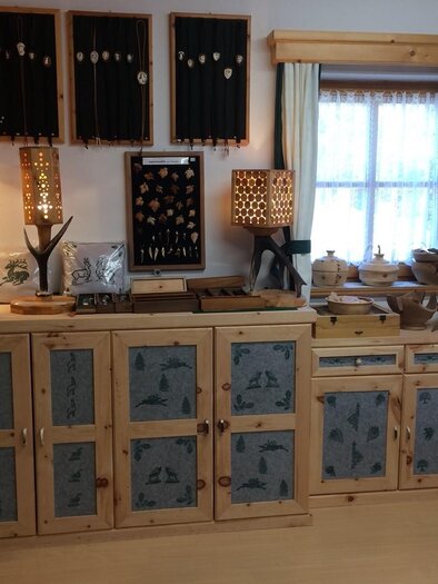 Eine Holzwerkstatt mit handgefertigten Holzgegenständen und Schmuck. Die Wände sind mit kunstvollen Holzschränken und Regalen dekoriert. | © Elisabeth Diethart