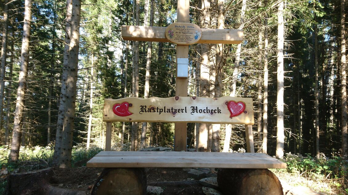 Ein ruhiger Rastplatz im Wald mit einem Holzkreuz und einer Bank. Der Platz ist umgeben von hohen Bäumen und vermittelt eine friedliche Atmosphäre. | © Schäffer