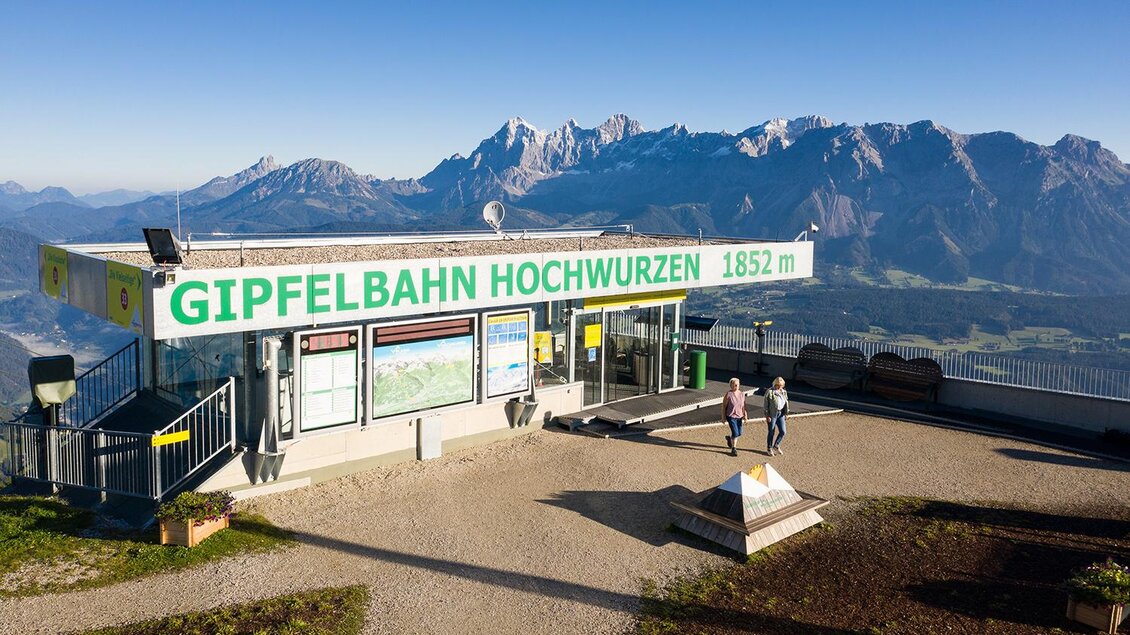 Eine Bergstation mit dem Namen „Gipfelbahn Hochwurzen“ befindet sich auf 1852 m Höhe. Im Hintergrund sind majestätische Berge und ein klarer Himmel zu sehen. | © Josh Absenger