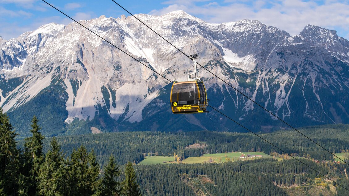 Eine Seilbahn fährt über eine schöne Berglandschaft. Die schneebedeckten Gipfel und grünen Wiesen sind sichtbar. | © Alexander Klünsner