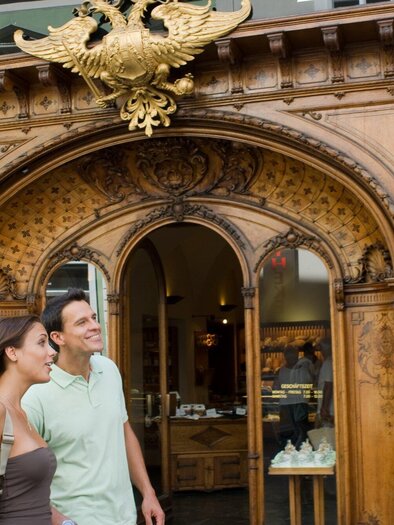 Ein paar lächelnde Personen stehen vor der eleganten Fassade einer Bäckerei. Die Tür und das Holzdesign sind kunstvoll verziert. | © Graz Tourismus - Hans Wiesenhofer