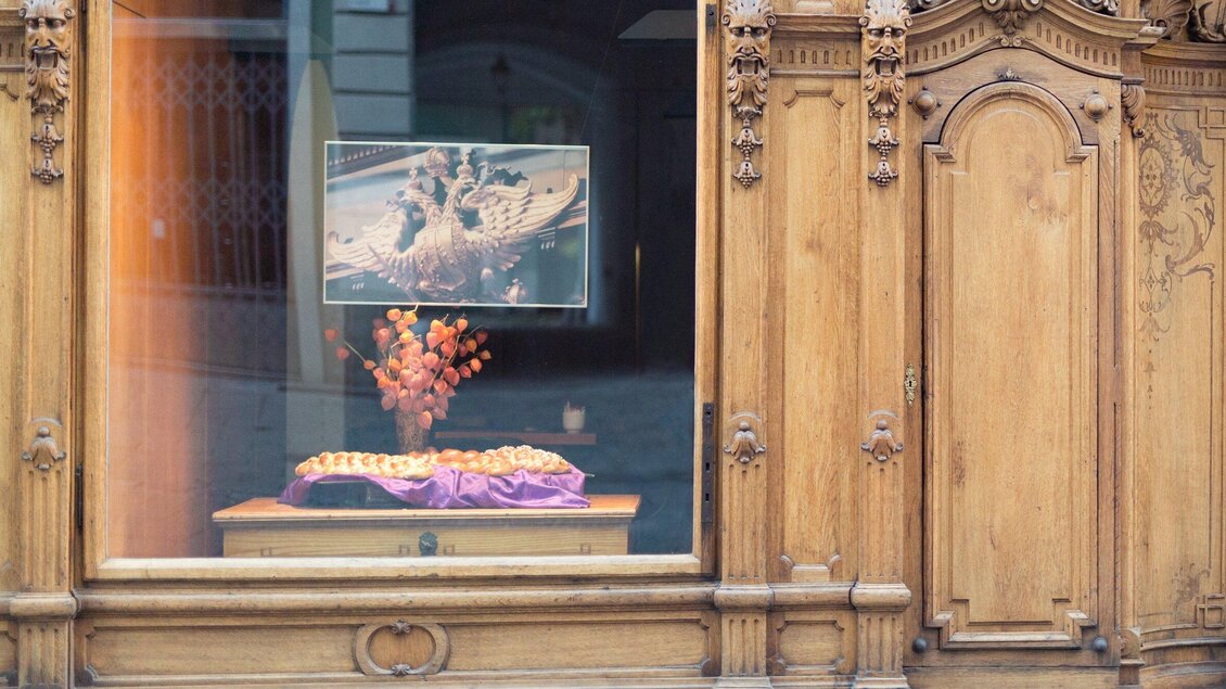 Ein Holzmöbelstück mit einer dekorativen Vitrine. Darin befindet sich ein Blumengesteck und ein Bild von Tänzern. | © Stiefkind Fotografie