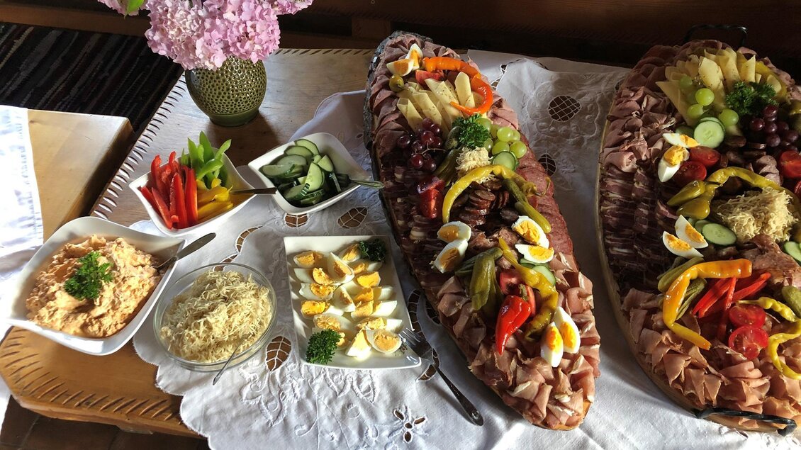 Ein reichhaltiges Buffet mit zwei großen Platten voller Wurst und Gemüse. Dazu sind verschiedene Salate und frische Beilagen angerichtet. | © Hofbauer Almhütte