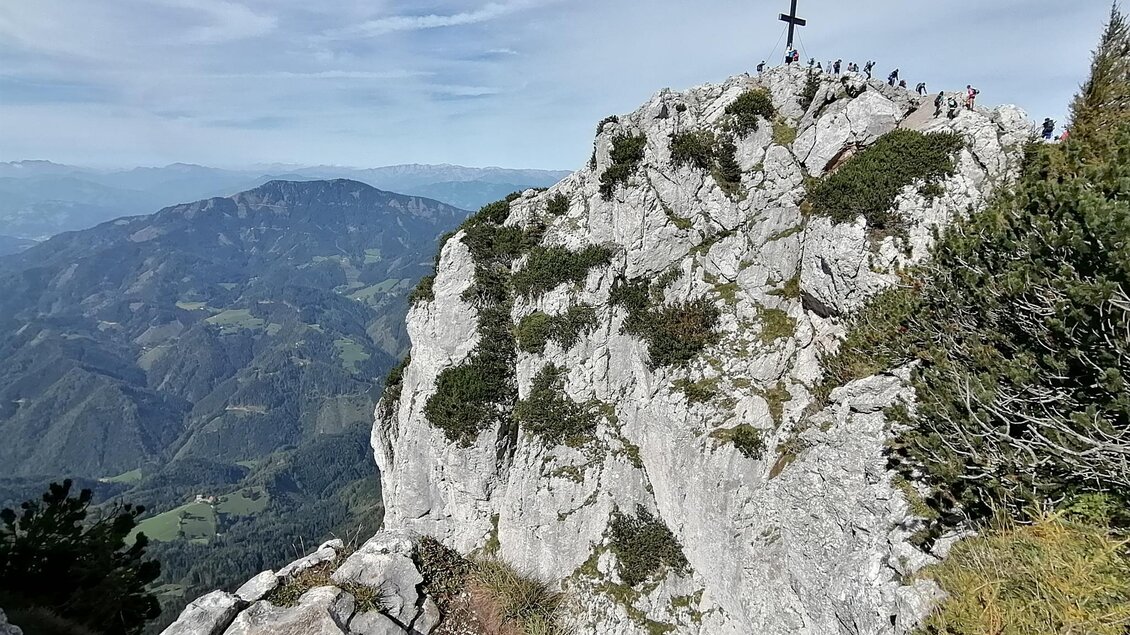 Ein beeindruckender Berggipfel mit einem Kreuz und zahlreichen Wanderern. Im Hintergrund erstreckt sich eine malerische Berglandschaft. | © Tourismusverband Oststeiermark