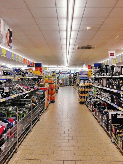 Ein Supermarktgang mit Regalen voller Produkte. Auf beiden Seiten sind Einkaufswagen und eine Vielzahl von Waren zu sehen. | © Symbolbild