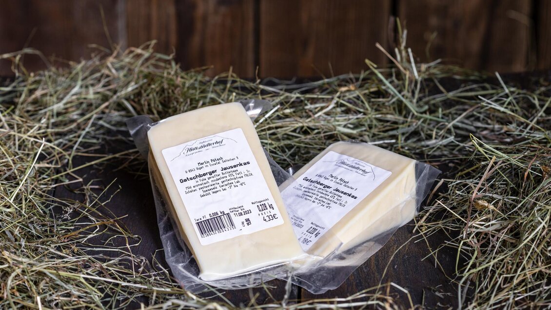 Zwei Stücke eingeschweißter Käse liegen auf einem Bett aus Heu. Die Verpackung zeigt die Produktinformationen klar an. | © Martin Huber
