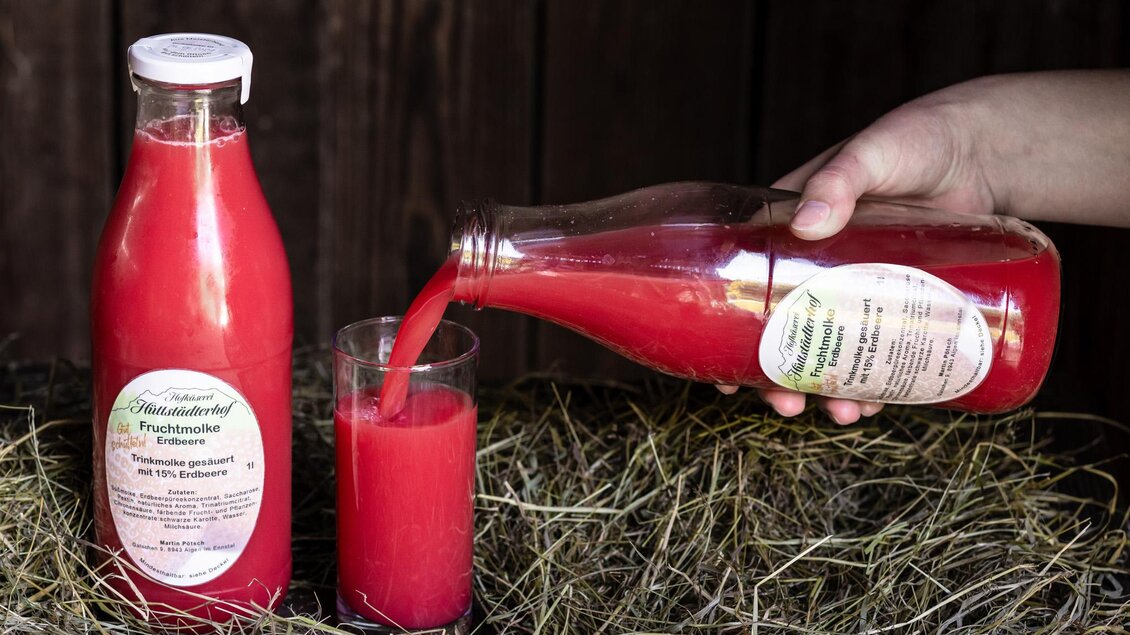 Ein Hand hält eine Flasche mit rotem Fruchtsaft, während er den Saft in ein Glas gießt. Im Hintergrund liegt Heu. | © Martin Huber