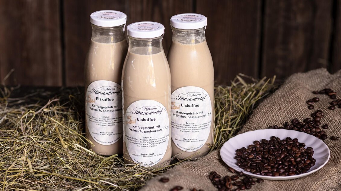 Drei Flaschen mit einer hellbraunen Getränkemischung stehen auf einer Heuunterlage. Neben den Flaschen liegt ein kleiner Teller mit Kaffeebohnen. | © Martin Huber
