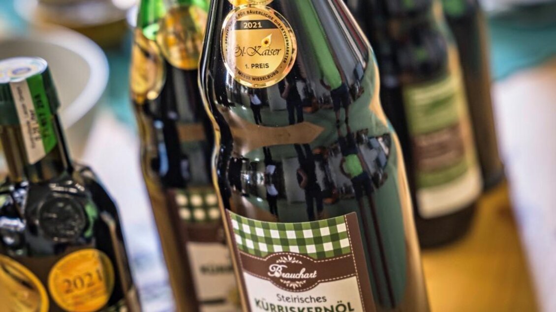 Eine Auswahl an Flaschen mit hochwertigen Kürbiskernöl auf einem Tisch. Die Flaschen sind mit Auszeichnungen und Etiketten versehen. | © Österreich Werbung/ Hans de Kort