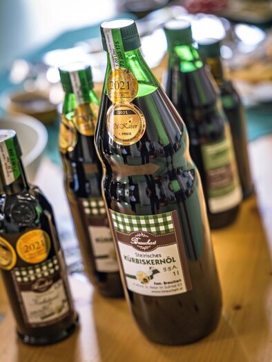 Eine Auswahl an Flaschen mit hochwertigen Kürbiskernöl auf einem Tisch. Die Flaschen sind mit Auszeichnungen und Etiketten versehen. | © Österreich Werbung/ Hans de Kort