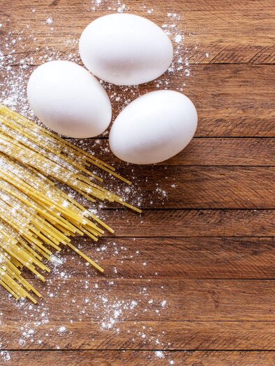 Ein Bündel Spaghetti und drei weiße Eier liegen auf einem Holzuntergrund. Darüber verstreut ist etwas Mehl. | © TV Südsteiermark - Adobe Stock