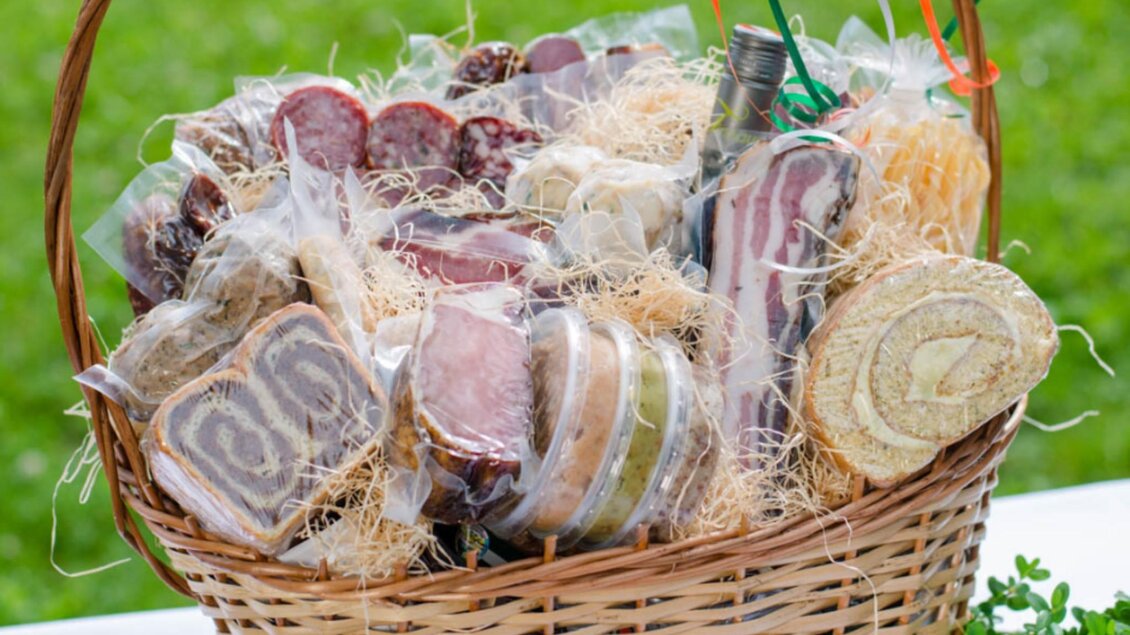 Ein Korb voller verschiedener Wurst- und Käseprodukte, hübsch verpackt und dekoriert mit Heu. Die Präsentation ist einladend und köstlich. | © Bauernhof König - Familie König