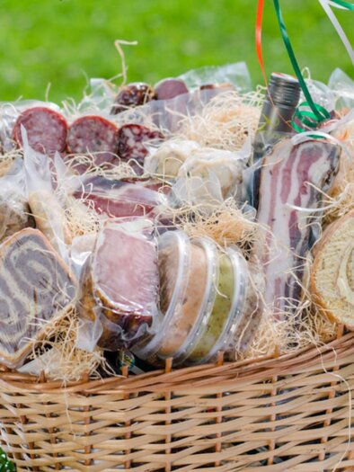 Ein Korb voller verschiedener Wurst- und Käseprodukte, hübsch verpackt und dekoriert mit Heu. Die Präsentation ist einladend und köstlich. | © Bauernhof König - Familie König