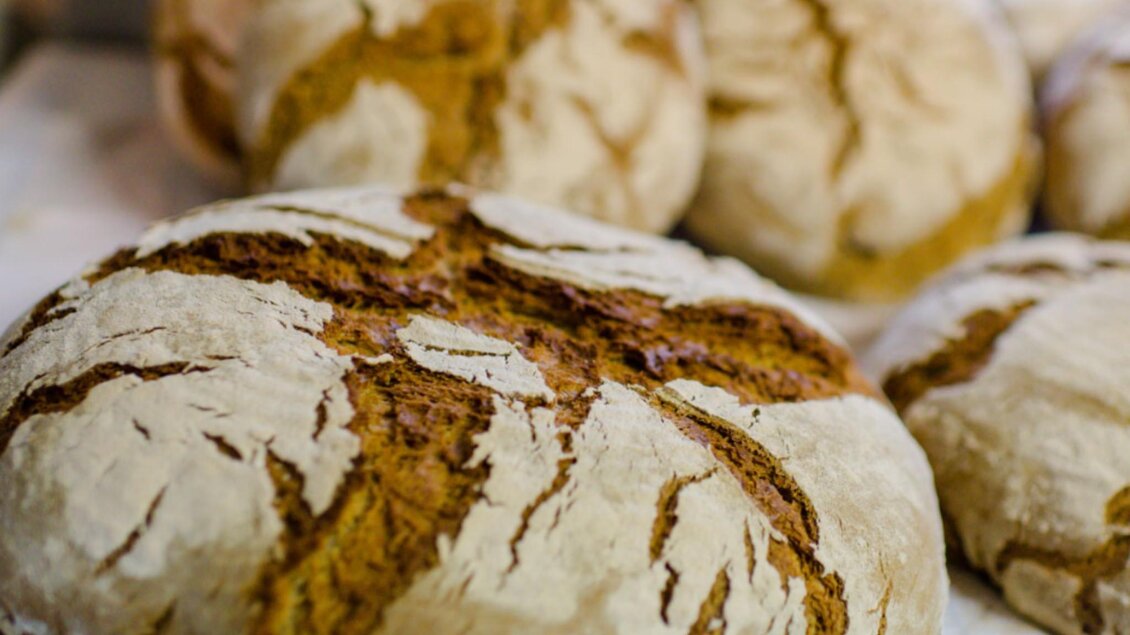 Ein frisches Brot mit einer knusprigen Rinde liegt im Vordergrund. Im Hintergrund sind weitere Brote sichtbar. | © Bauernhof König - Familie König