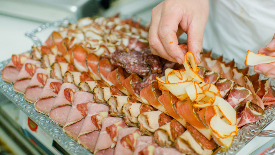 Eine dekorative Platte mit verschiedenen Wurst- und Schinkensorten, kunstvoll angerichtet. Eine Hand platziert sorgfältig dünne Scheiben von Apfel auf die Wurstplatte. | © Bauernhof König - Familie König