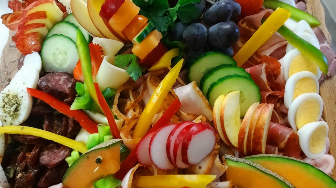 Eine bunte Platte mit verschiedenen Wurst- und Käseaufschnitten, frischem Gemüse und Obst. Die Anordnung ist ansprechend und einladend. | © Sigrid Burkart