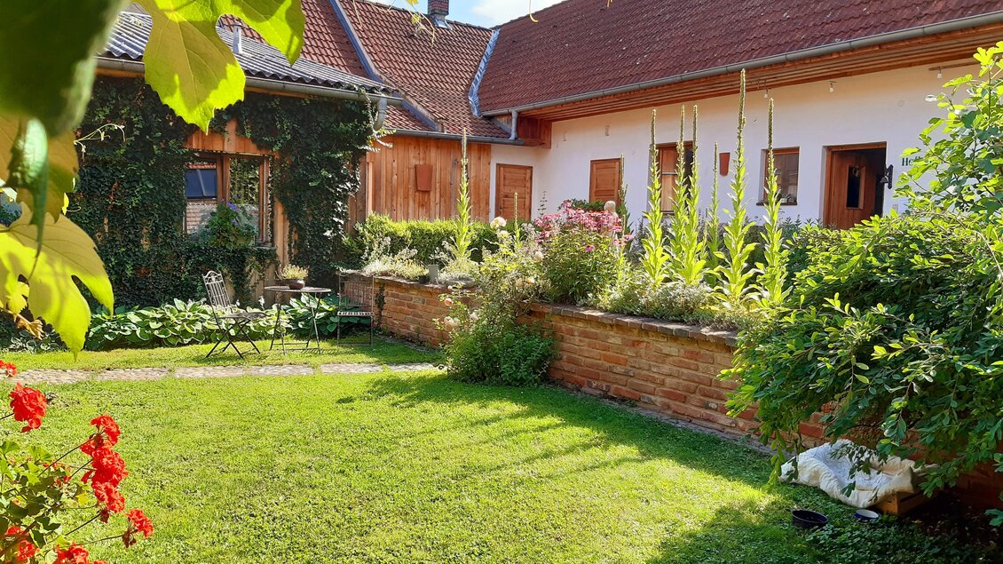 Ein schöner Garten mit grünem Rasen und bunten Blumen. Im Hintergrund sind Häuser mit roten Dächern zu sehen. | © Familie Brugner